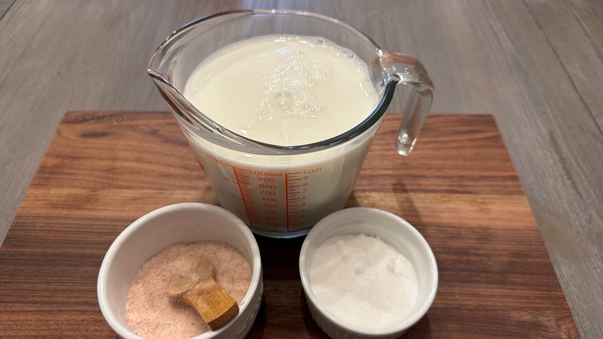 Ingredients for homemade lactose-free condensed milk: milk in a measuring cup, sugar, and cinnamon in small bowls.