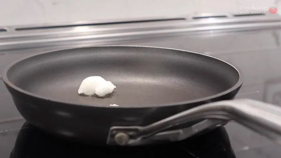 Coconut oil melting in a dark pan on stovetop for roasting peanuts and spices.