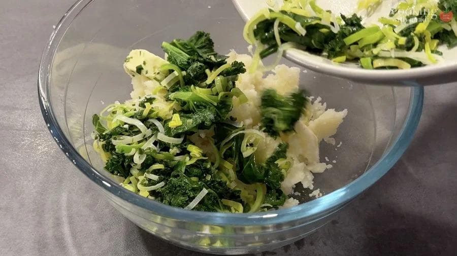 Mashed potatoes mixed with chopped green onions and chives in a glass bowl during preparation.