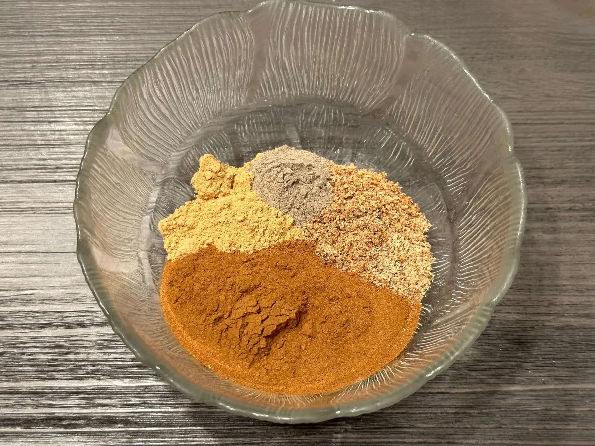 Four ground spices mixed together in a clear glass bowl: turmeric, cinnamon, ginger, and allspice for apple pie spice.