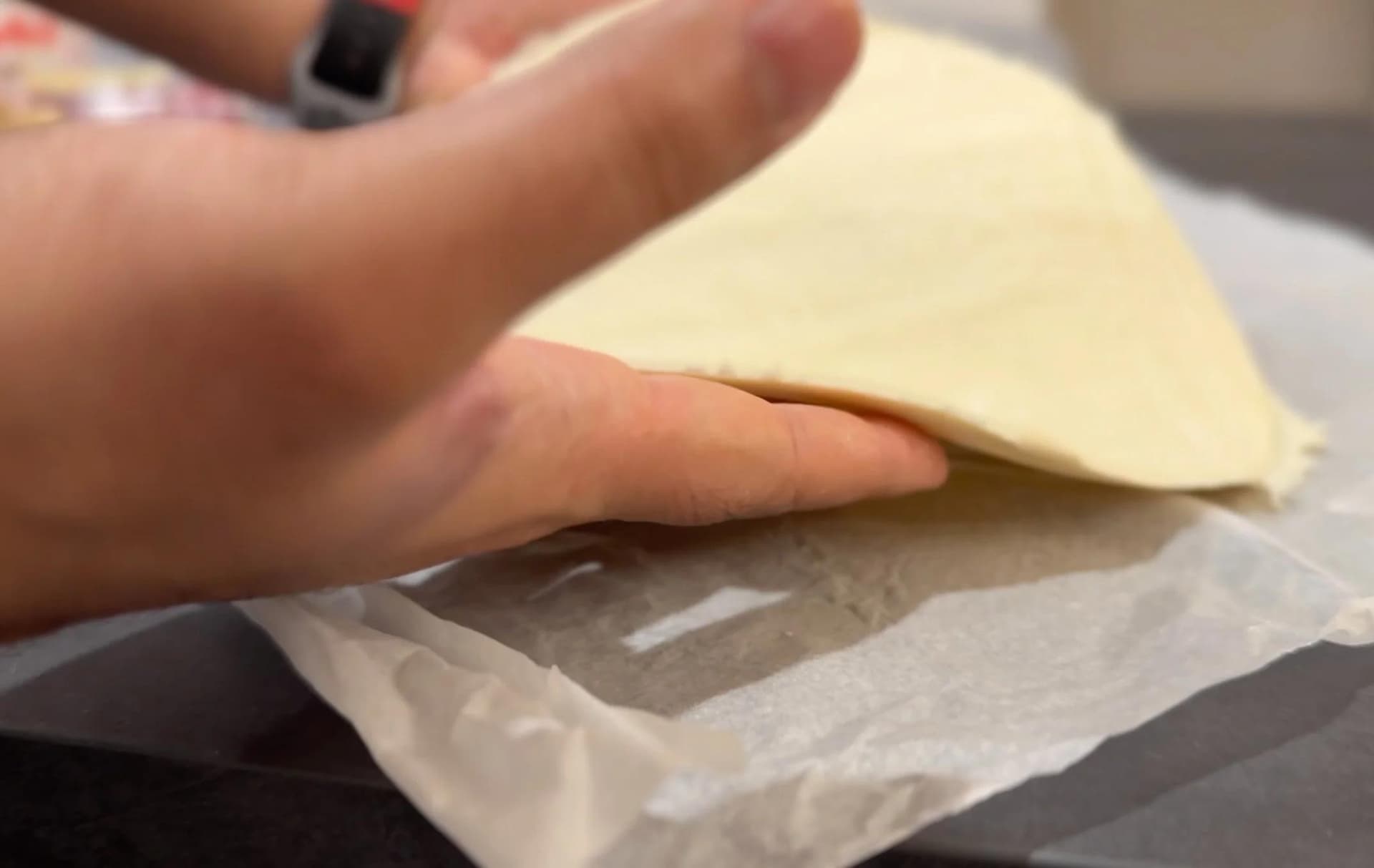 Hand folding the edge of a circular puff pastry sheet on parchment paper to create a galette rim.