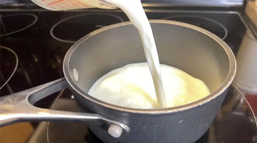 Milk being poured into a saucepan on the stovetop for heating during red velvet latte preparation.
