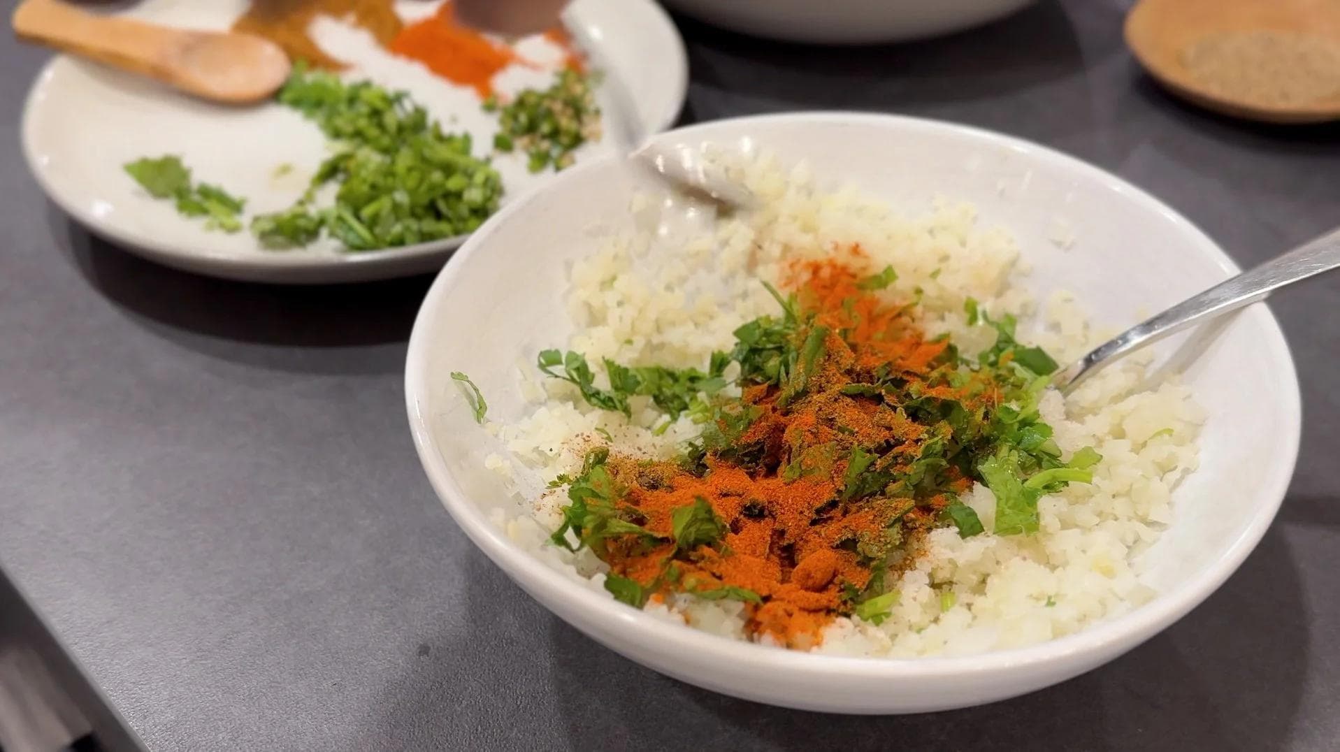 Riced cauliflower mixed with cilantro, green chilies, and spices in a white bowl with a spoon.