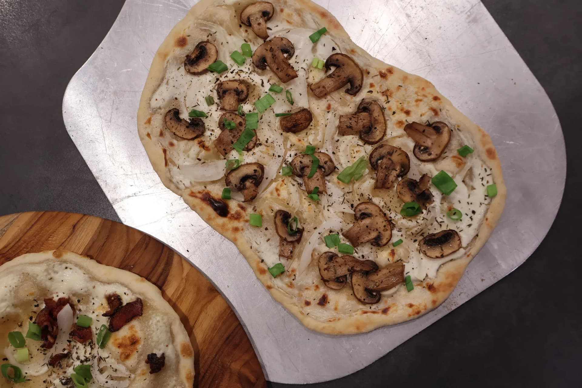 Baked flammkuchen with sautéed mushrooms, melted cheese, and fresh green onions on parchment paper.
