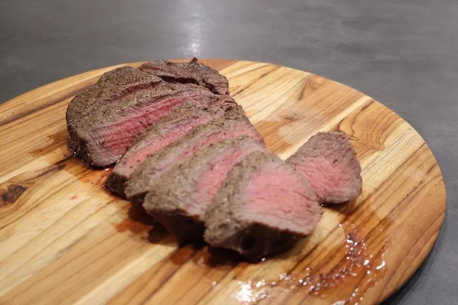 Sliced medium-rare sirloin steak on a wooden cutting board showing pink center and juices.