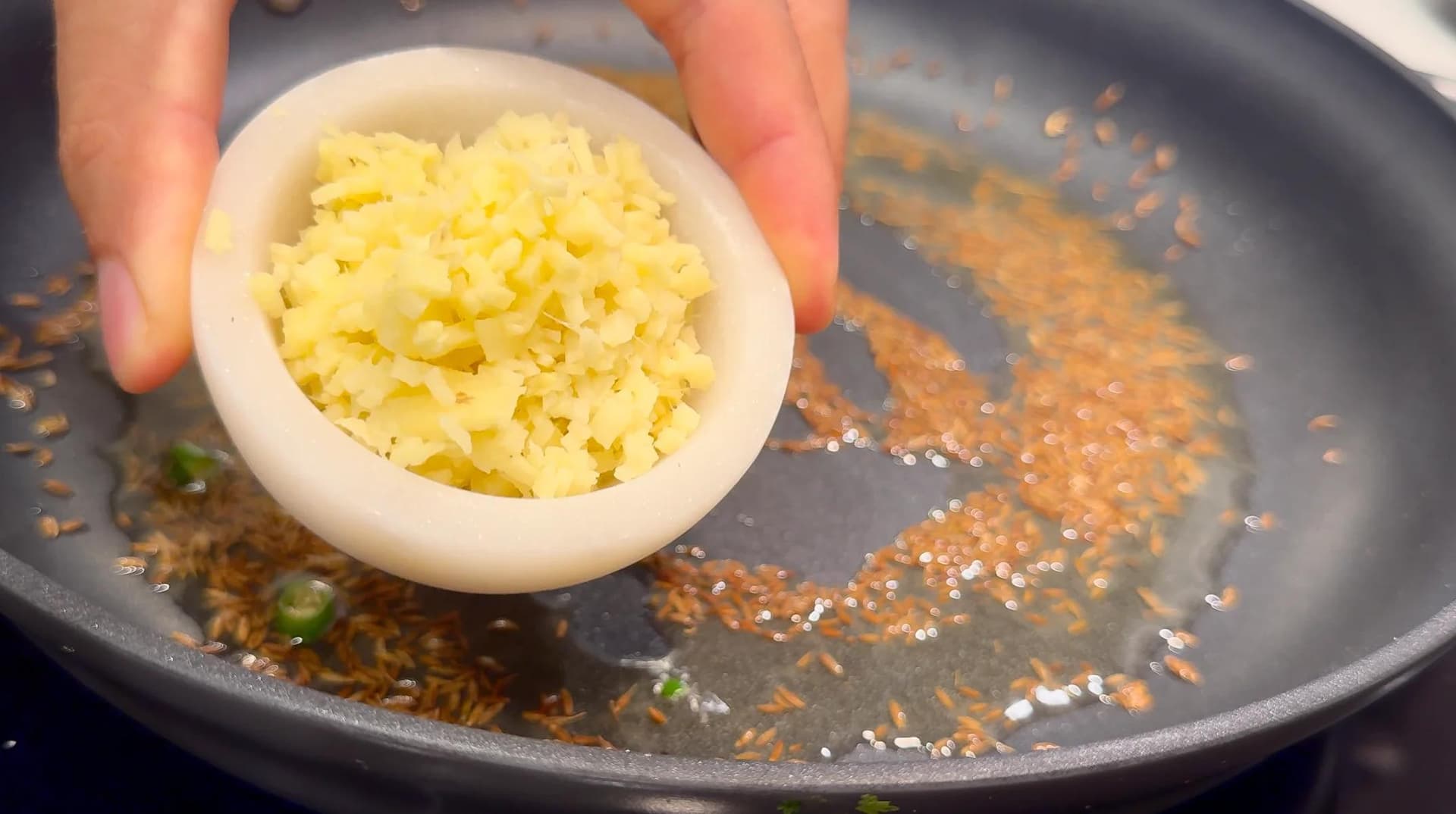 Mashed potatoes being added to a pan with toasted cumin seeds and spices for samosa filling.