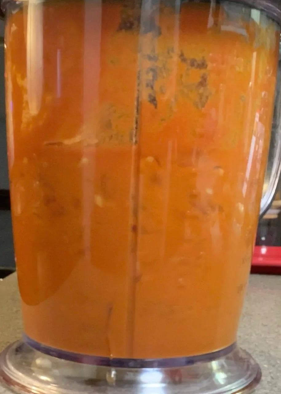 Smooth tomato-based sauce in a blender, orange-red in color, ready for cooking Shahi Paneer.