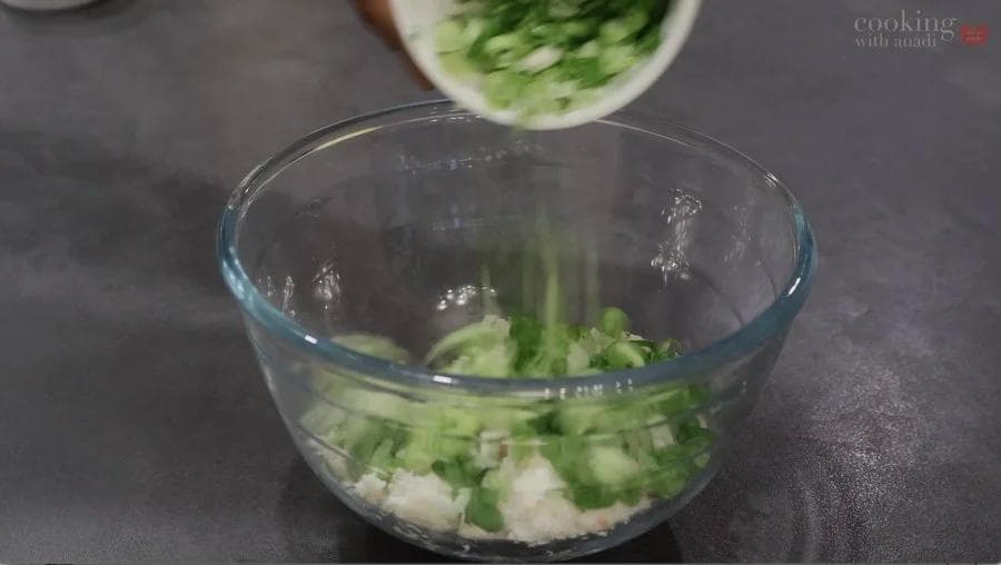 Green onions and white crab meat being added to a glass bowl during preparation of crab salad.