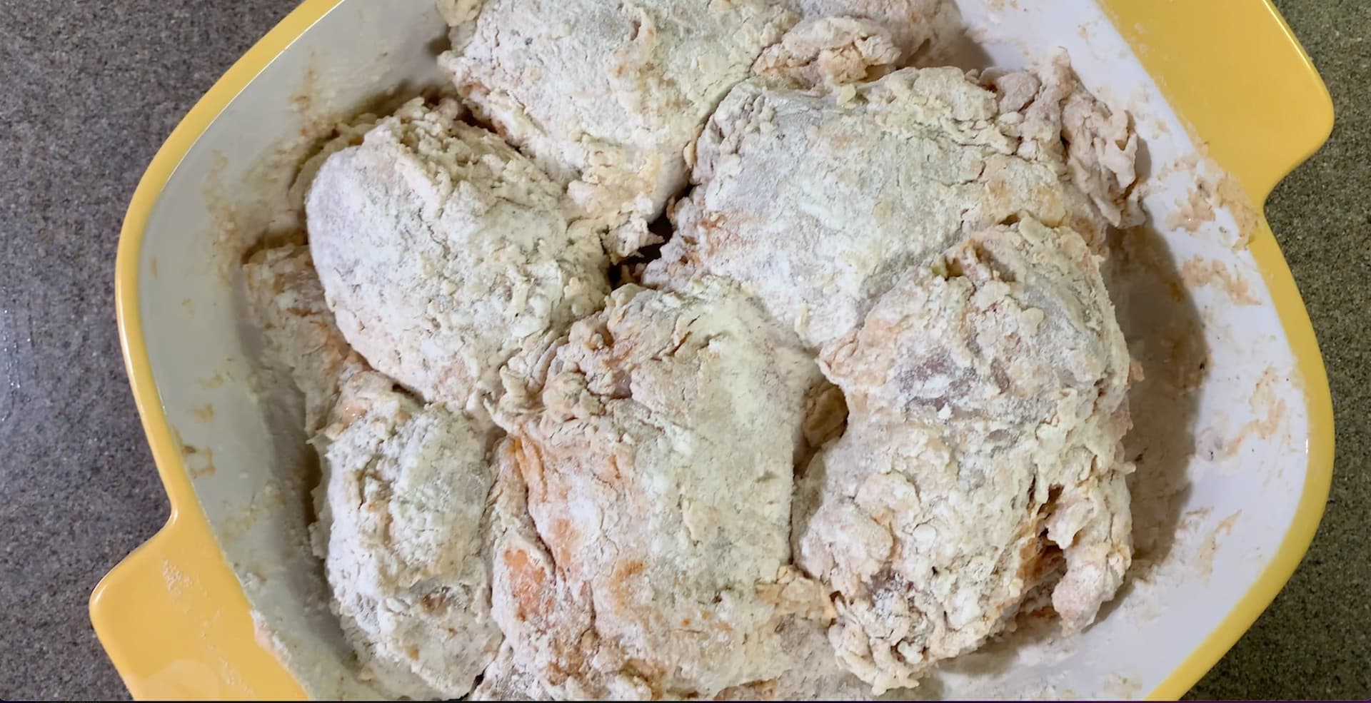 Chicken pieces coated in seasoned flour in a yellow bowl, ready for frying.