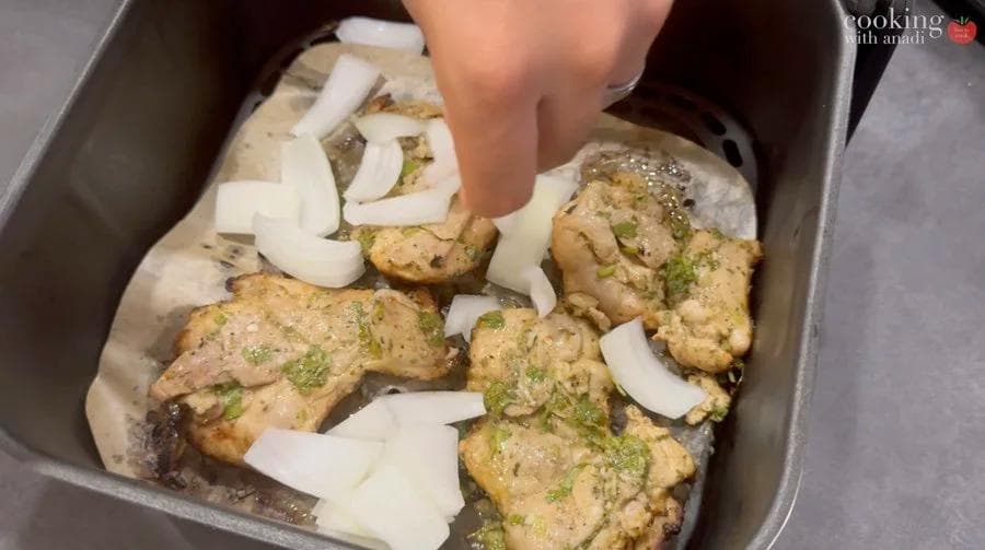 Cooked mojo chicken thighs with sliced onions in an air fryer basket, garnished with fresh cilantro.