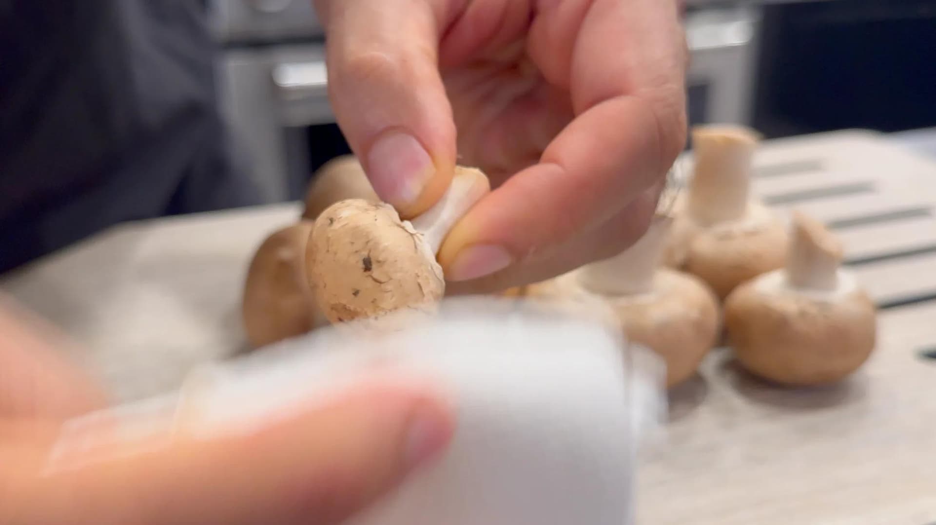Hand holding a cooked mushroom over a white bowl with sautéed mushrooms and onions during krokiety filling preparation.
