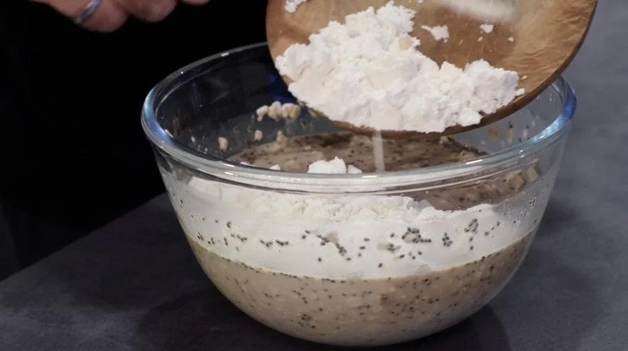 Pouring white powder into a bowl of mixed oats and ingredients for tiramisu overnight oats.