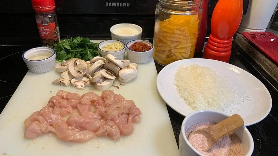 Ingredients for spicy creamy chicken penne laid out on a counter including diced chicken breast, mushrooms, pasta, garlic, and seasonings.