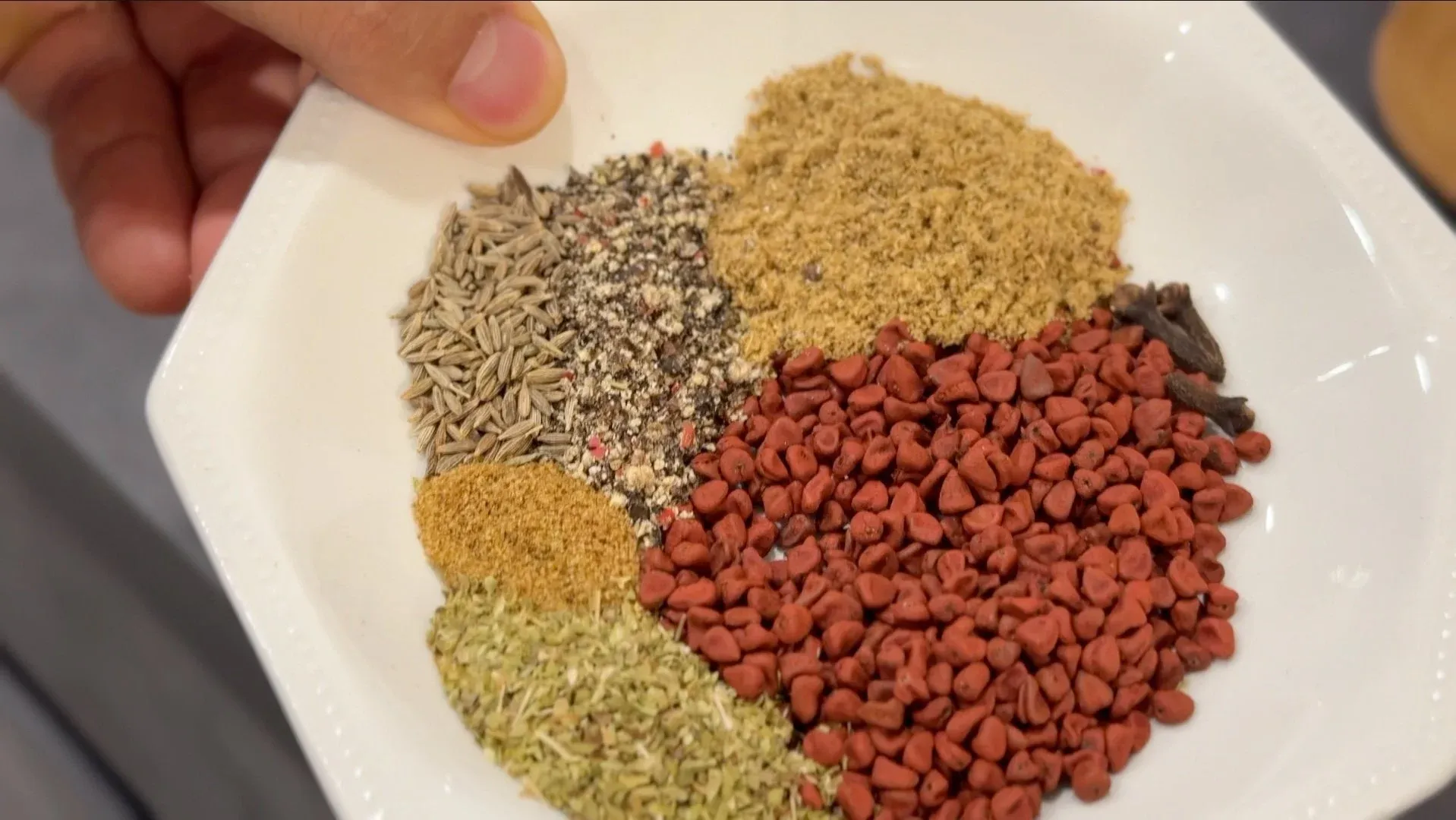 Spices and seasonings arranged on a white plate for making recado paste: sunflower seeds, poppy seeds, ground cumin, achiote, dried oregano, and red pepper flakes.