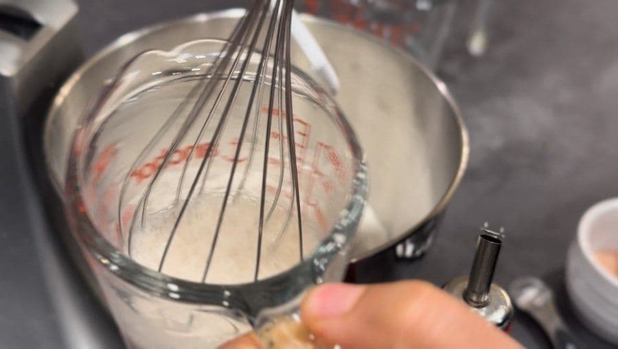 Whisking yeast and lukewarm water in a glass measuring cup until bubbly for pizza dough.