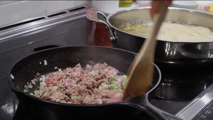 Ground meat mixture with shallots and green onions being stirred in a black skillet on stovetop.
