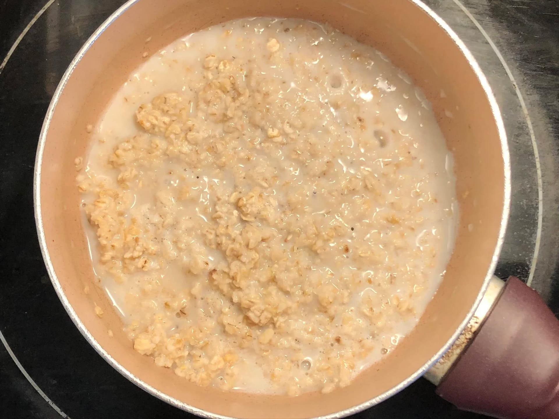 Oatmeal simmering in a pot with milk, showing a creamy beige mixture with visible oat pieces.