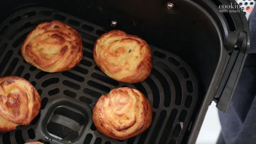 Golden-brown mashed potato pinwheels arranged in an air fryer basket during cooking.