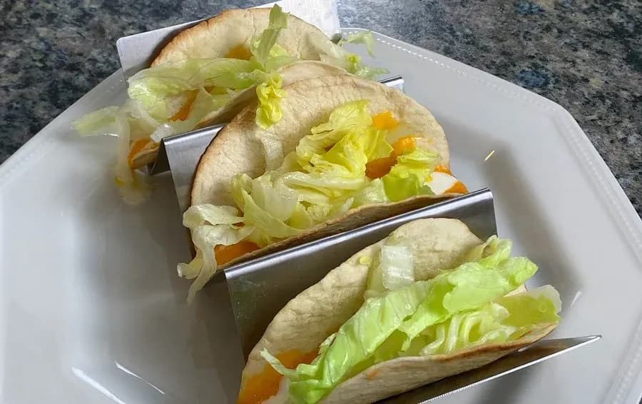 Three crispy chicken and shrimp tacos topped with shredded lettuce and diced tomatoes on a white plate.