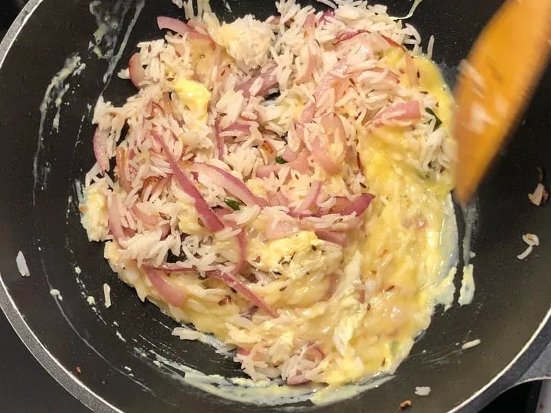 Scrambled eggs mixed with shredded chicken and ham in a dark skillet, mid-stir with a wooden spoon.