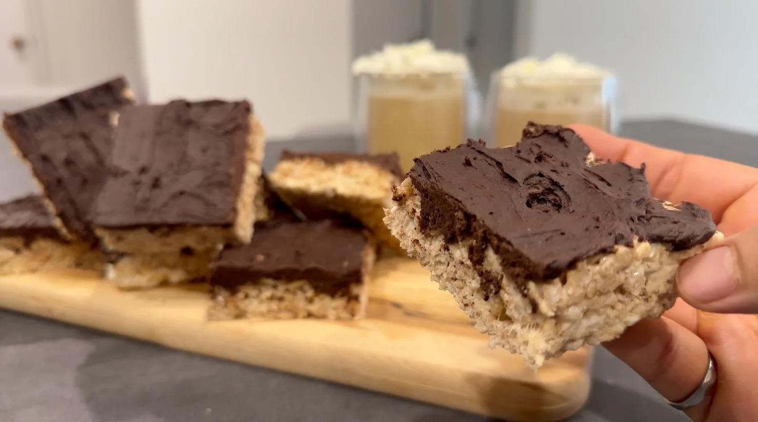 Protein Rice Krispies treats with chocolate topping, held in hand, showing layered cereal and chocolate coating.