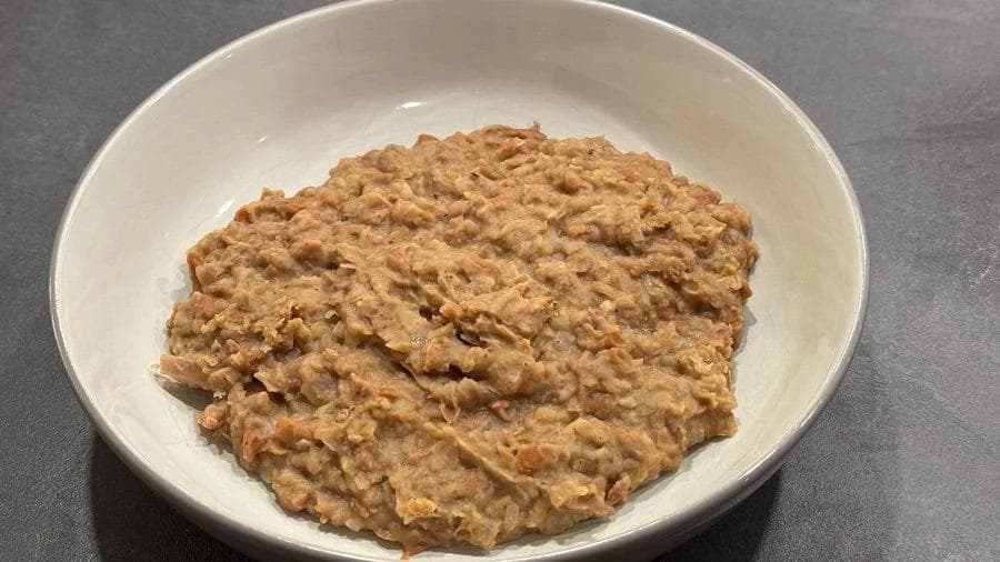 Homemade refried beans in a white bowl, showing a thick, creamy brown texture with a chunky consistency.