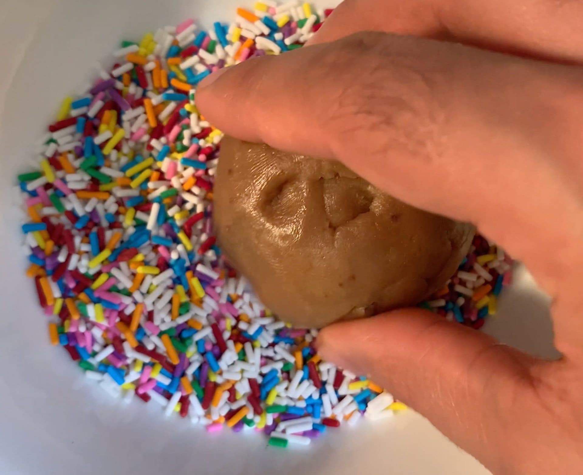 Hand pressing chocolate cookie dough coated in colorful rainbow sprinkles