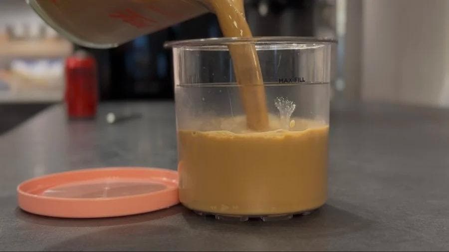 Ginger chai mixture being poured into a Ninja Creami container with a coral lid on a kitchen counter.