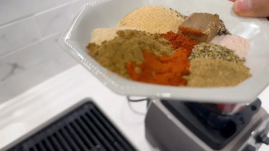 Dried spices including garlic powder, onion powder, cumin, paprika, and cayenne pepper measured in a white bowl.