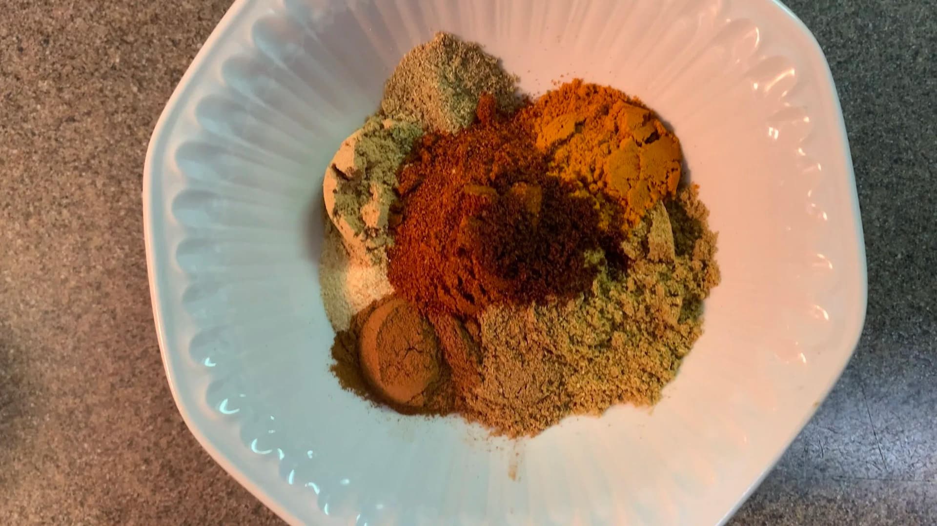 Freshly mixed Indian curry powder spice blend on a white plate, showing turmeric, cinnamon, coriander, and paprika.