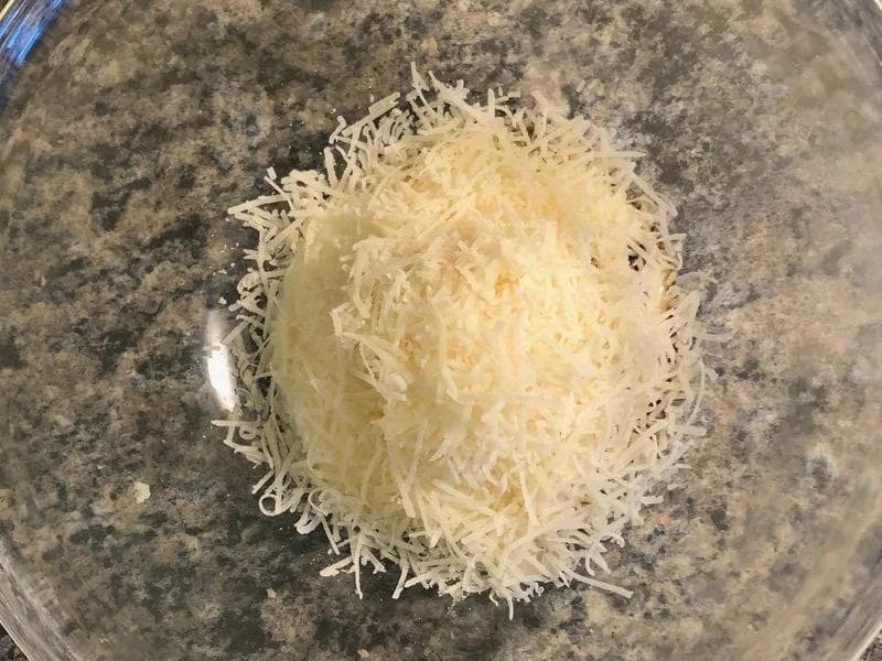 Shredded Parmesan cheese piled in a glass bowl before mixing into Greek yogurt Caesar dressing.