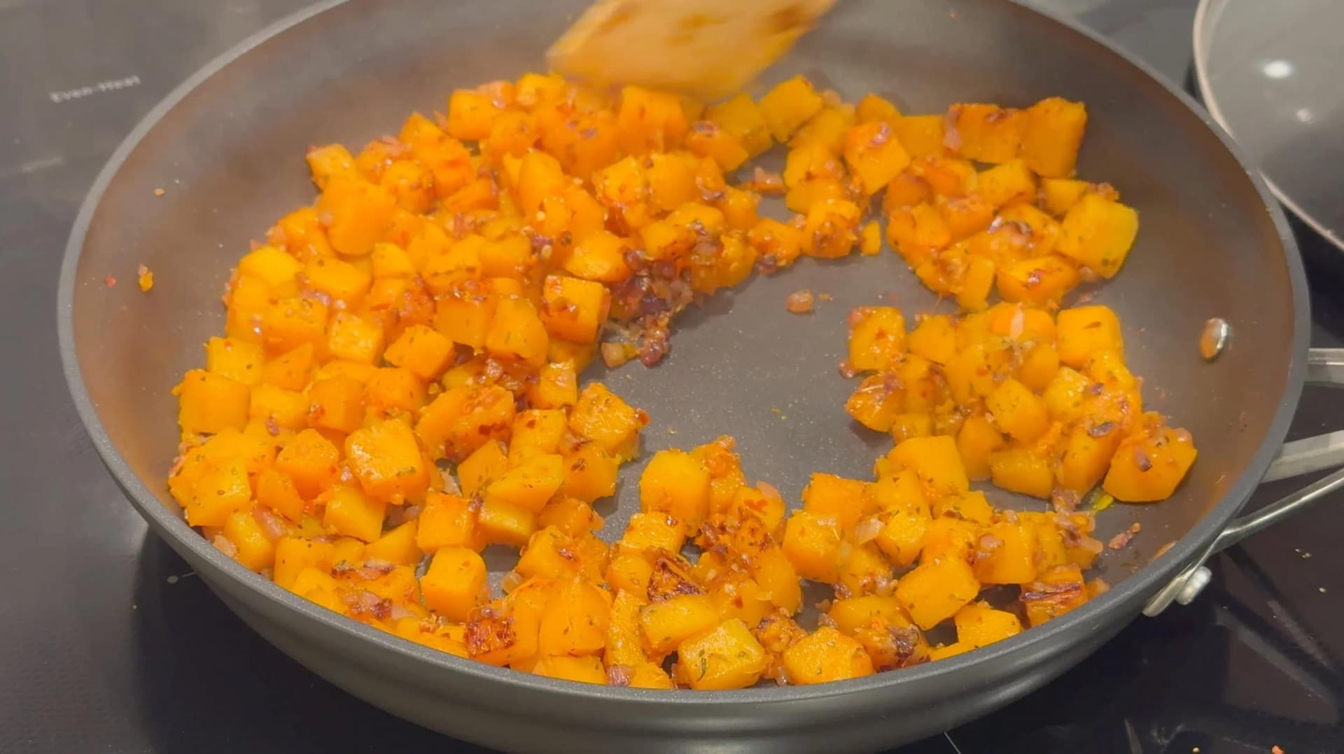 Diced butternut squash cooking in a pan with brown seasoning and caramelized edges.
