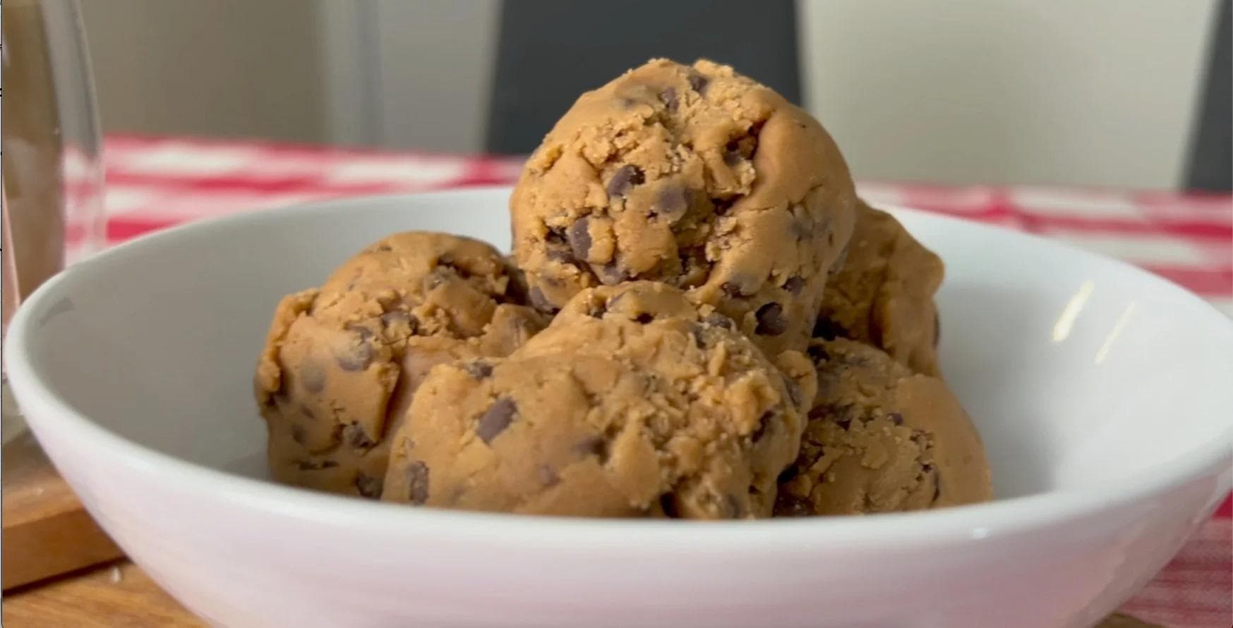 Three scoops of chocolate chip cookie dough in a white bowl on a striped pink and white cloth.