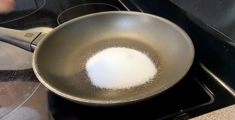 Sugar and water mixture simmering in a wok on a stovetop during caramel sauce preparation.