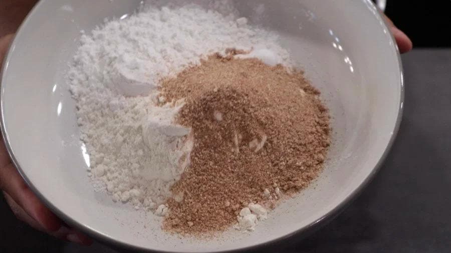 Dry breading mix with flour and brown seasoning powder combined in a white bowl.
