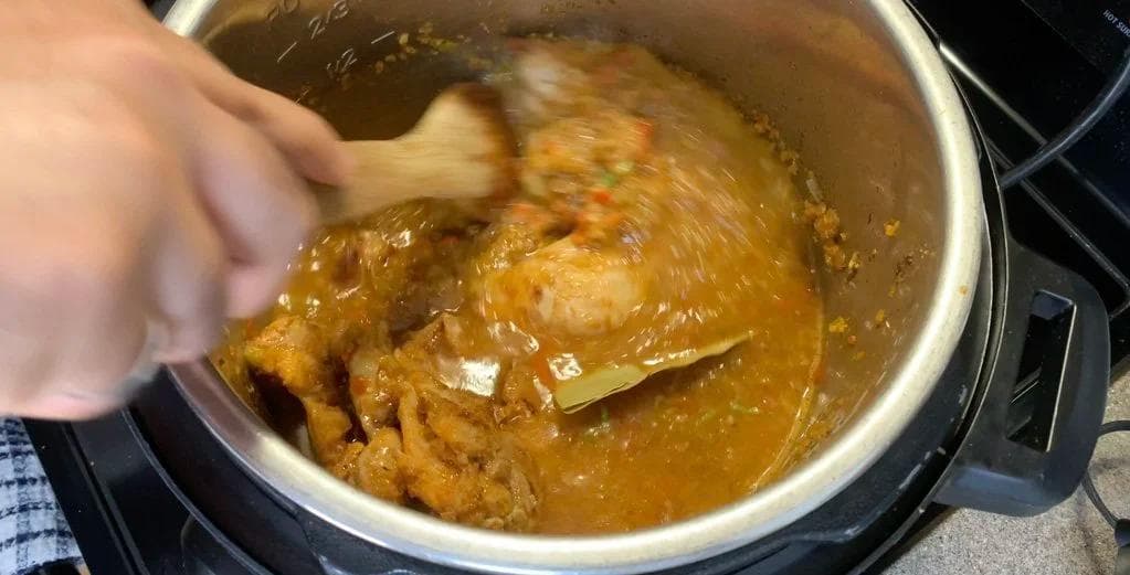 Hand stirring chicken and spiced sauce in Instant Pot before pressure cooking arroz con pollo.