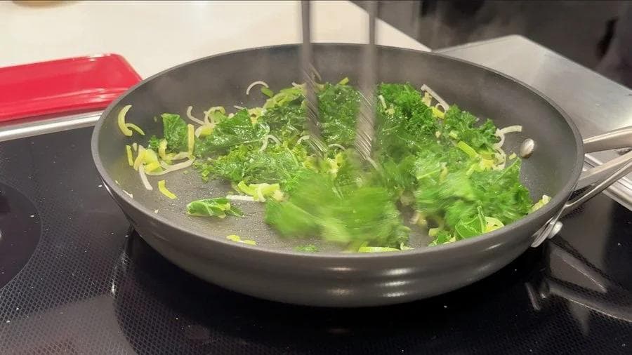 Sautéed leeks and kale wilting in a dark skillet with garlic-chive butter over medium heat.