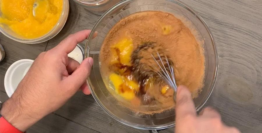 Whisking pumpkin pie filling with eggs, condensed milk, and coffee in a glass bowl.