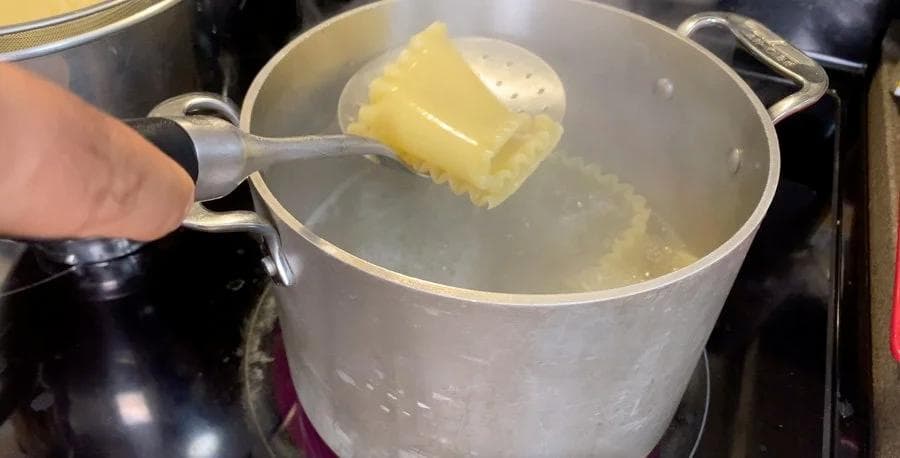 Butter being added to a pot of boiling water for cooking lasagna sheets.