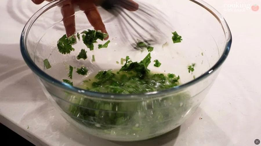Cilantro and garlic mojo marinade being whisked together in a glass bowl with citrus juice and olive oil.