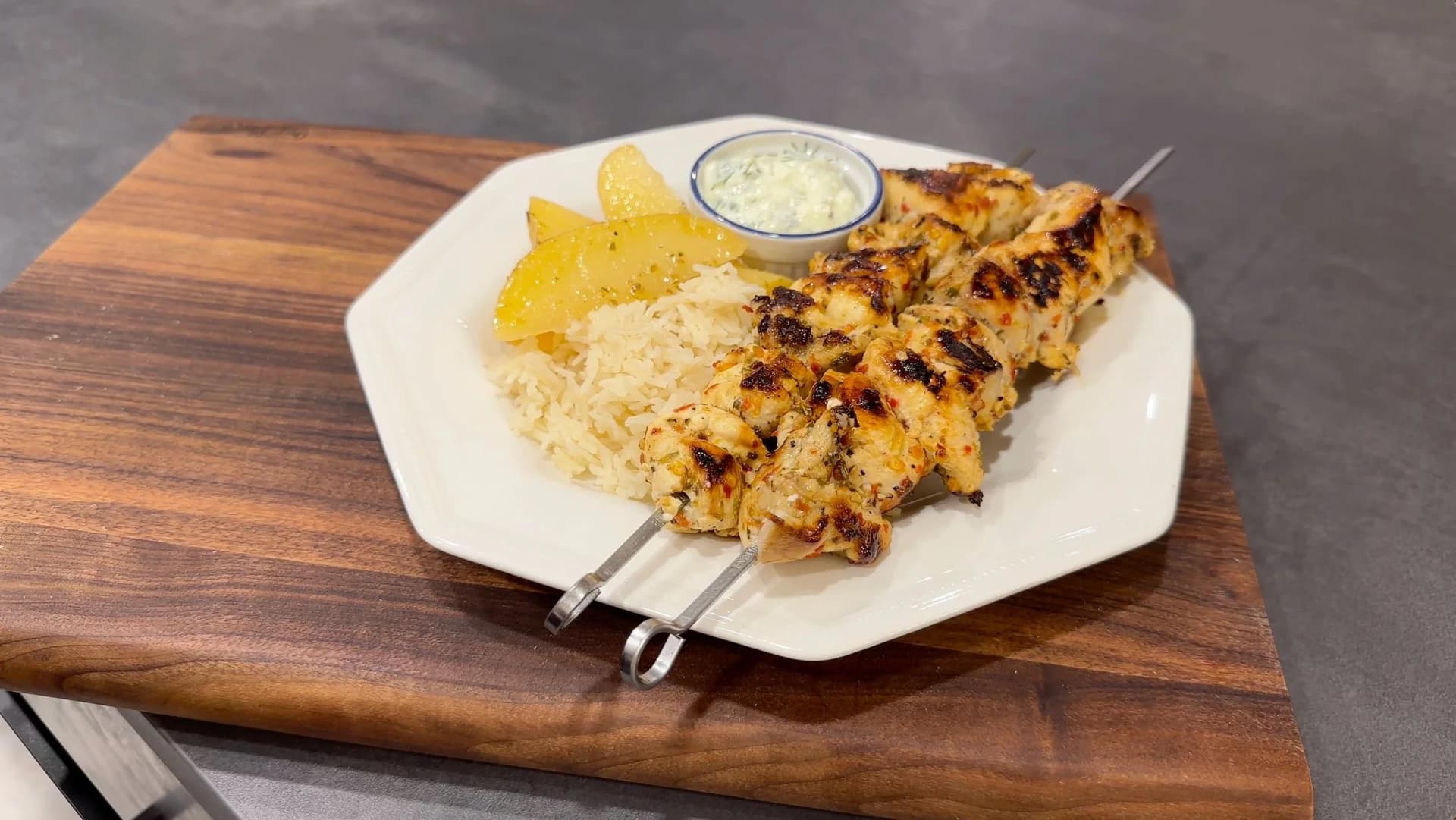Grilled Greek chicken souvlaki skewers served with lemon rice, lemon potatoes, and tzatziki sauce on a white plate.