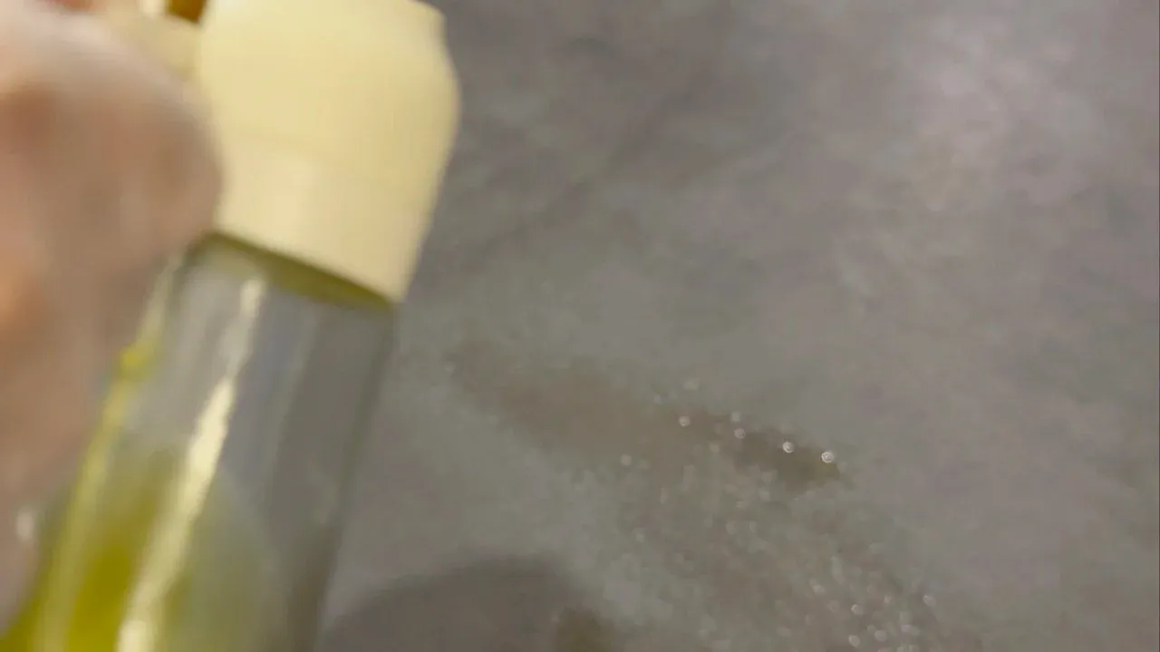 Oil being sprayed onto a work surface with a spray bottle during momo dough preparation.