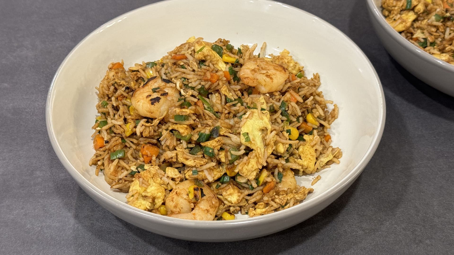 Shrimp fried rice with eggs, vegetables, and green onions served in a white bowl.