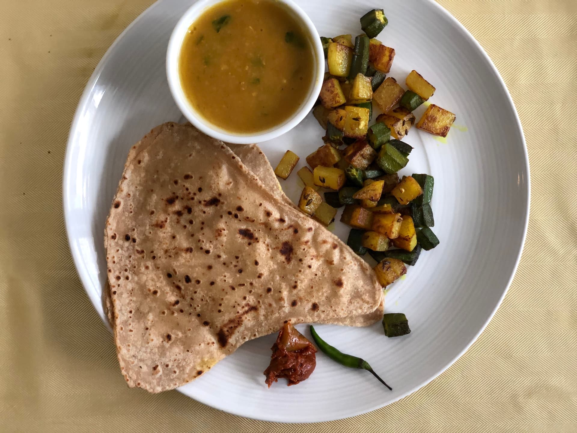 Plated crepes with crispy okra and potato curry, served with gravy in a white bowl on a white dish.
