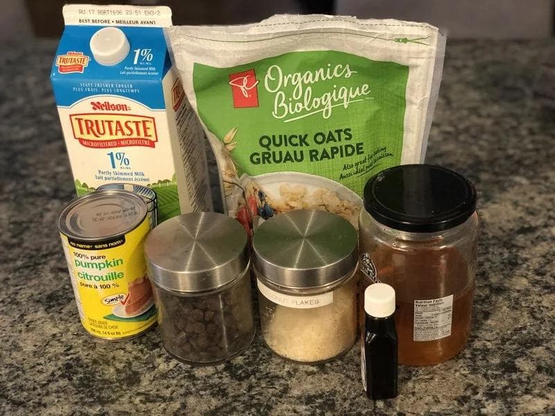 Ingredients for pumpkin oatmeal: milk carton, canned pumpkin, quick oats, chocolate chips, coconut flakes, vanilla, and honey.