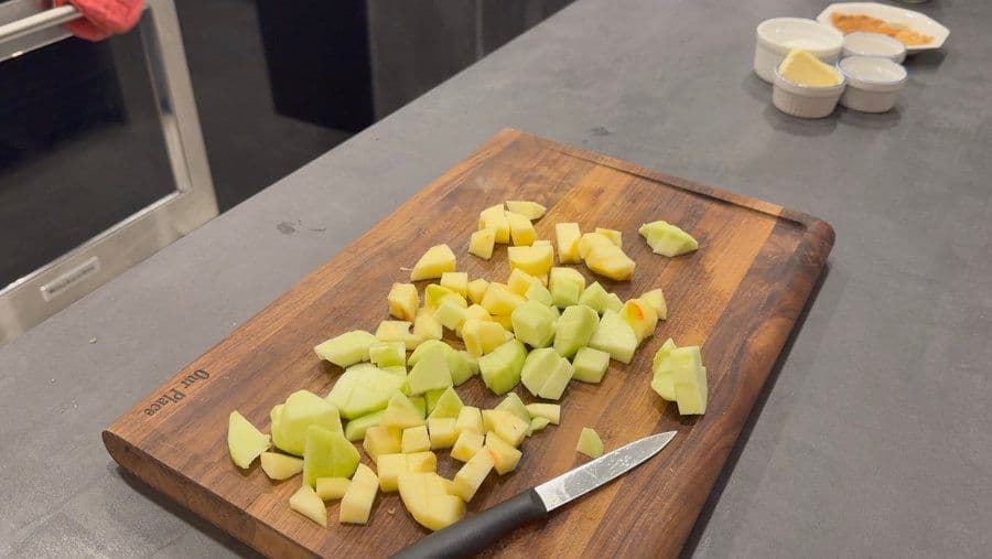 Diced apples on a wooden cutting board with a knife, prepared for apple pie filling.