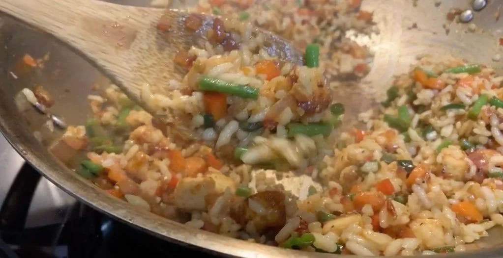 Spicy paneer fried rice being tossed in a wok with green onions, carrots, and paneer chunks visible throughout.