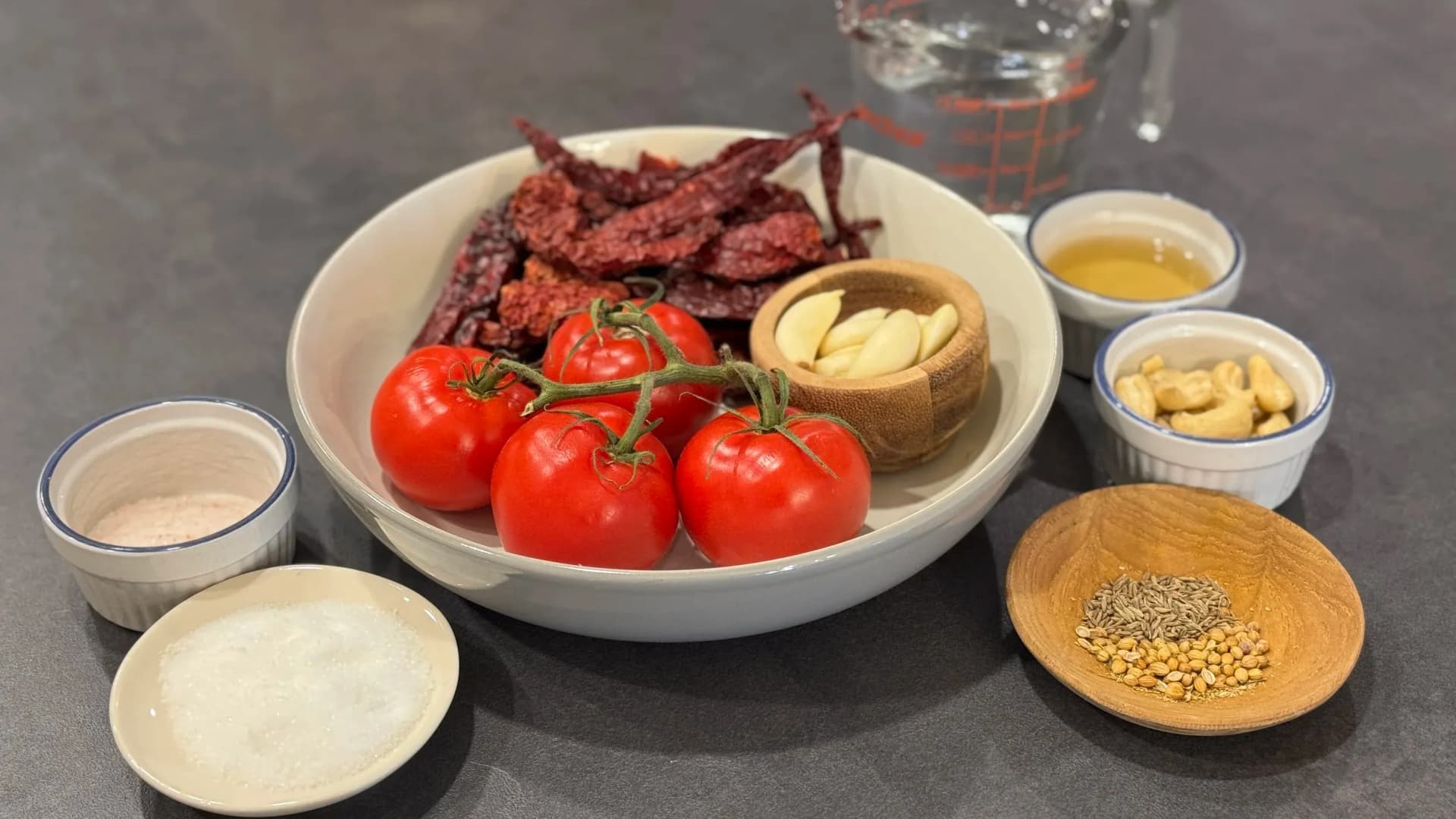Ingredients for spicy momos chutney laid out including fresh tomatoes, dried red chilies, garlic, peanuts, and various condiments in bowls.