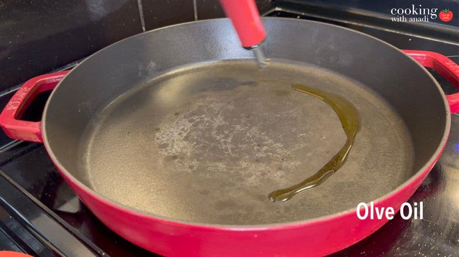 Hot pink cast-iron pan with olive oil heating on stovetop for cooking chicken.