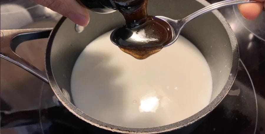 Pouring vanilla bean paste from a spoon into a pan of warm milk for a French vanilla cappuccino.